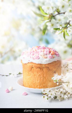Traditioneller Osterkuchen mit weißem schweizer Meringue und rosafarbener Dekoration und bunten bemalten Eiern auf Hintergrund blühende Kirsch- oder Apfelgarten fl Stockfoto