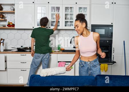Fröhliches multikulturelles Paar in gemütlicher Hauswäsche, das während der Frühjahrsputz zu Hause arbeitet Stockfoto