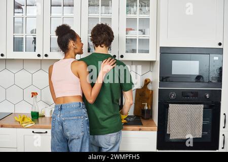 Eine hübsche afroamerikanerin, die glücklich ihren liebenden Freund ansieht, der seine Hausaufgaben macht Stockfoto
