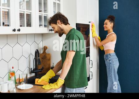 Fröhlich multikulturell schönes Paar in Hauswäsche, das ihre Arbeit während der Frühjahrsputz macht Stockfoto