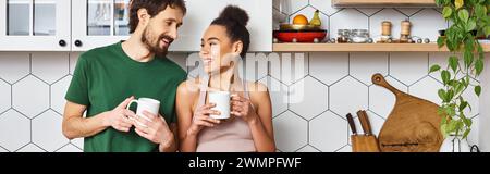 Attraktives, abwechslungsreiches Paar in Homewear, das heissen Kaffee genießt und sich ansieht, Banner Stockfoto