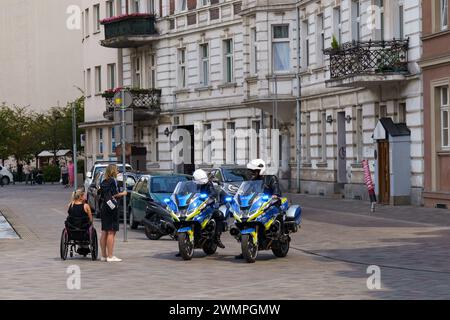 Posen, Polen - 18. Juni 2023: Polnische Polizeibeamte auf Motorrädern sprechen mit einer behinderten Frau im Rollstuhl und ihrem Freund auf einem Platz auf einem hellen Stockfoto