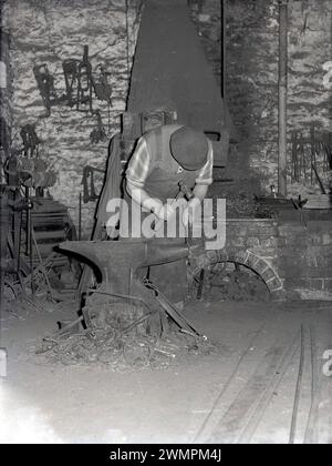 1960er Jahre, historisch, ein Schmied oder Farrier, der an einem Hufeisen an einem Amboss arbeitet, in einer Schmiede, England, Großbritannien. Stockfoto