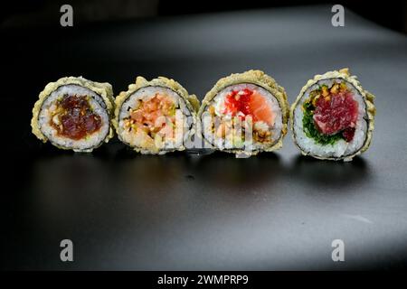 Verschiedene Sushi-Brötchen mit Sauce und Belag auf dunkler Tischplatte Stockfoto