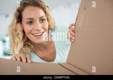 Neugierig lächelnde junge Frau, die das Paket auspackt Stockfoto
