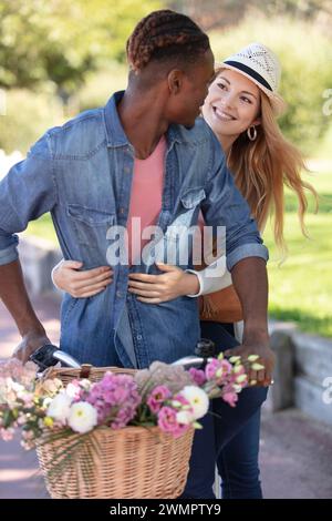 Lachende junge Paare, die auf einer sonnigen Straße Fahrrad fahren Stockfoto