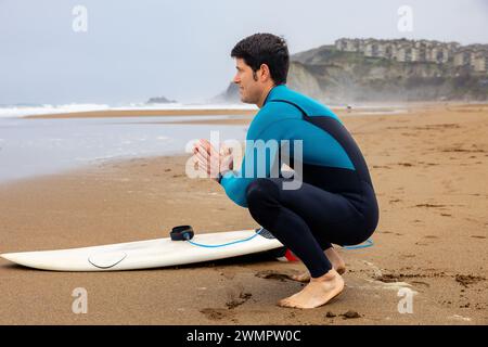 Junger Athlet, der vor dem Meer elastisch sitzt, bevor er die Wellen fängt. Stockfoto