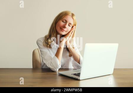 Müde überarbeitete die schlafende Frau, während sie mit einem Laptop arbeitete und morgens am Schreibtisch im Büro saß Stockfoto