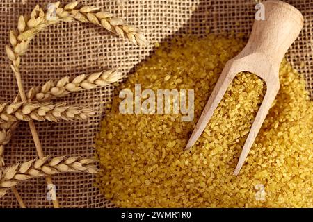 Hölzerne Schaufel auf einem Haufen trockenen Bulgur-Hartweizen mit Weizenohren auf Sackleinen Stockfoto