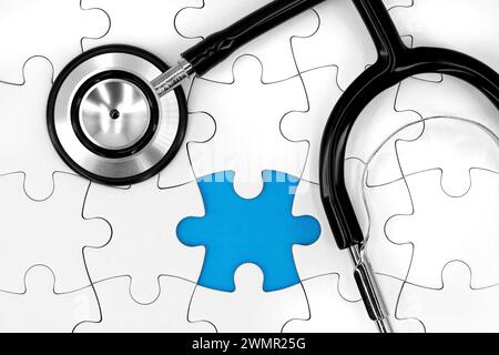 Schwarzes Stethoskop auf weißem Puzzle mit fehlendem Stück und blauem Kopierraum, medizinisches Konzeptbild Stockfoto
