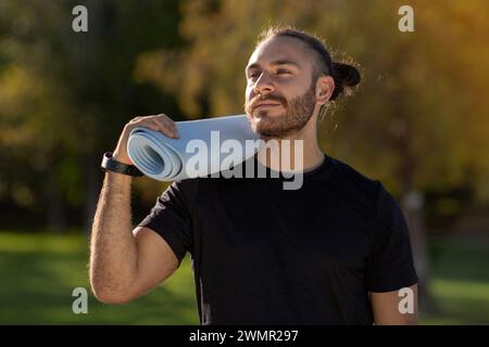 Junger athletischer Mann in Sportbekleidung, der Fitness-Matte im Freien trägt Stockfoto