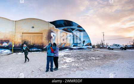 Touristen machen Fotos vor dem farbenfrohen Wandgemälde an der Außenseite der Eisbärenhaltestelle in Churchill, Manitoba bei Sonnenaufgang. Stockfoto