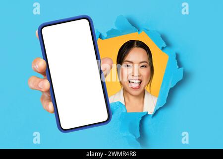 Lächelnd aufgeregte junge asiatische Dame mit offenem Mund, die Handy mit leerem Bildschirm zeigt Stockfoto
