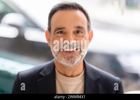 Fröhlicher Geschäftsmann mit grauem Bart und hellem Lächeln in schwarzer Jacke Stockfoto