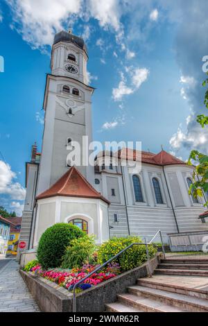 Nesselwang, Deutschland - 06. Juli 2023: Weitwinkel-Nordansicht der St. Andreas-Kirche mit Glockenturm und Blumenbeeten vor blauem Himmel mit Wolken. Stockfoto