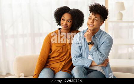 Ein zufriedenes afroamerikanisches Paar sitzt dicht auf einem Sofa, die Frau lehnt sich in den Mann Stockfoto