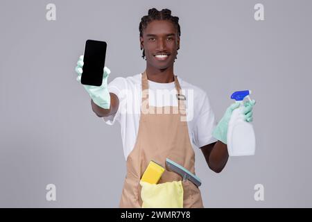 Reinigungsservice-Anzeige. Schwarzer Mann Mit Schürze, Der Ein Leeres Smartphone In Der Hand Zeigt Stockfoto