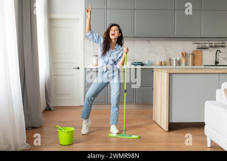 Fröhliche junge Frau tanzt mit Mopp in stilvoller Küche Stockfoto