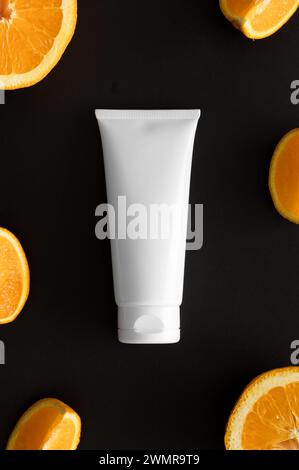 Blick von oben auf eine Tube Creme umgeben von Orangen auf schwarzem Hintergrund. Stockfoto