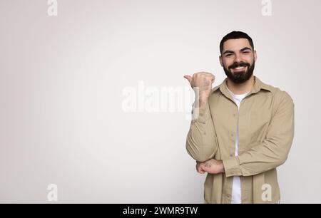 Fröhlicher bärtiger Mann, der ein Schild mit dem Daumen nach oben gibt und selbstbewusst in einem lässigen beigefarbenen Hemd lächelt Stockfoto