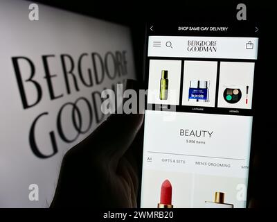 Person, die ein Mobiltelefon hält, mit Webseite des US-amerikanischen Luxus-Kaufhausunternehmens Bergdorf Goodman Inc. Mit Logo. Konzentrieren Sie sich auf die Mitte des Telefondisplays. Stockfoto