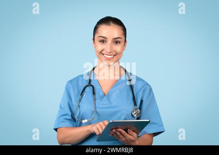 Aufmerksame Krankenschwester in Peelings mit Tablet lächelnd in die Kamera Stockfoto