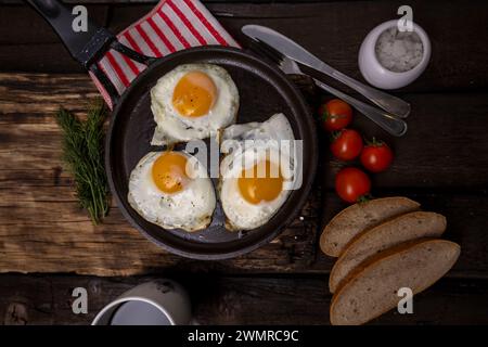 Spiegeleier in einer Pfanne mit Gemüse und Kräutern auf schwarzem Hintergrund Stockfoto