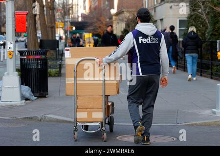 Ein FedEx-Mitarbeiter mit einem Handwagen voller Pakete, der über eine Straße läuft, New York, NYC. Stockfoto