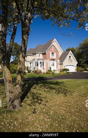 Zweistöckiges Haus aus rotem Backstein und brauner Verkleidung mit angelegtem Vorhof und Asphalteinfahrt im frühen Herbst. Stockfoto