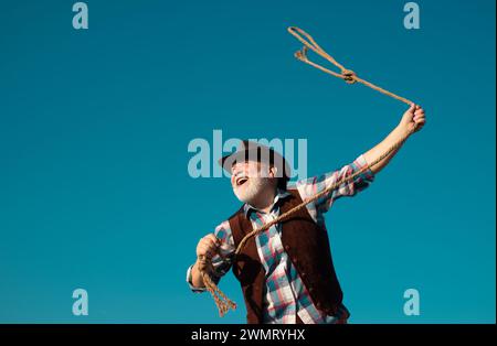 Lasso werfen. Alter Wilder Westen Cowboy mit Seil. Bärtiger Westernmann mit brauner Jacke und Hut, der Pferd oder Kuh fängt. Stockfoto