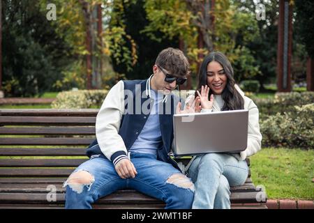 lateinische und kaukasische Studenten mit Kopfhörer und Laptop, die Videoanrufe auf dem Universitätsgelände machen Stockfoto