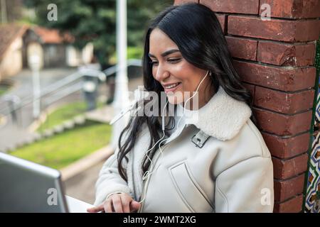 Nahaufnahme junges, brünettes lateinamerikanisches Mädchen, das Kopfhörer trägt und draußen mit Laptop arbeitet Stockfoto