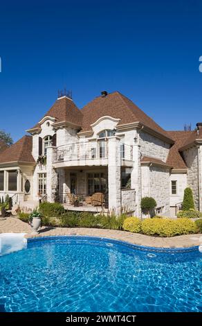 Im Erdgeschoss Swimmingpool im Hinterhof eines luxuriösen zweistöckigen hellen Steinhauses mit landschaftlich gestaltetem Hinterhof im Sommer. Stockfoto