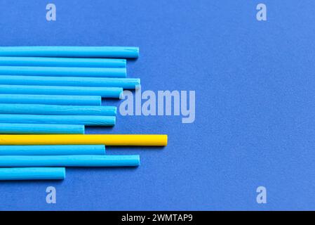 Ein gelber Stab unter blauen Stangen auf farbigem Hintergrund. Das Konzept der Einzigartigkeit Stockfoto