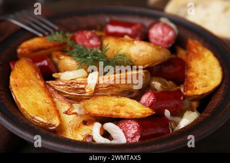 Leckere gebackene Kartoffel mit dünnen trockenen geräucherten Würstchen und Zwiebeln in Schüssel, Nahaufnahme Stockfoto