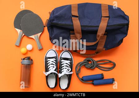 Sporttasche mit Sportbekleidung und Tischtennisausrüstung auf orangem Hintergrund Stockfoto