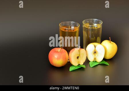 Zwei transparente Glasgläser mit verschiedenen Fruchtsäften auf schwarzem Hintergrund, neben jeder Hälfte reifer roter und gelber Äpfel. Nahaufnahme. Stockfoto