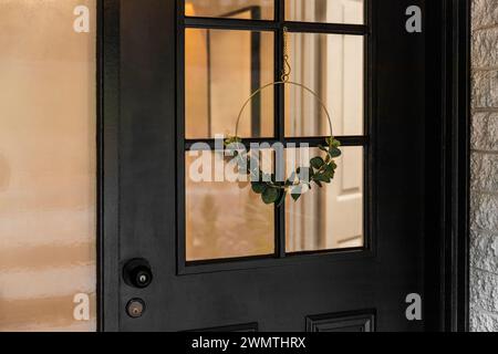 Nahaufnahme einer schwarzen Tür mit minimalistischem Dekorkranz. Stockfoto
