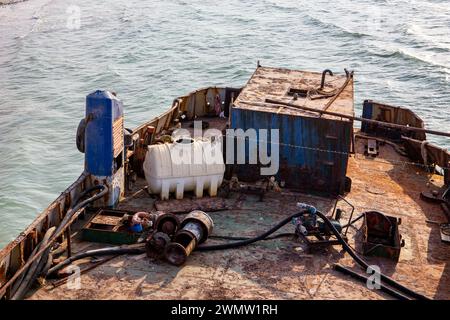 Zerstörtes und rostiges Deck eines Frachtschiffes, das an Land gewaschen wurde, mit alten Seilen, Rohren, Maschinen und Ausrüstung, am Strand von Al Hamriyah in Umm Al Quw Stockfoto