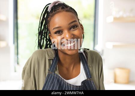 Eine junge Afroamerikanerin lächelt warm und trägt eine gestreifte Schürze Stockfoto