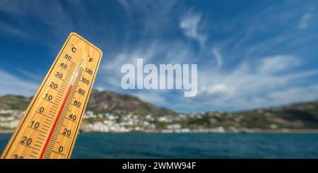 Holzthermometer mit roter Messflüssigkeit, die hohe Temperaturen an sonnigem Tag vor dem Hintergrund des Meeres anzeigt. Konzept von Urlaub, Urlaub, warmes Wetter Stockfoto