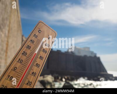 Holzthermometer mit roter Messflüssigkeit, die hohe Temperaturen an sonnigem Tag vor dem Hintergrund des Meeres anzeigt. Konzept von Urlaub, Urlaub, warmes Wetter Stockfoto