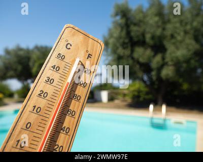 Holzthermometer mit roter Messflüssigkeit, die hohe Temperaturen an sonnigen Tagen auf dem Hintergrund des Schwimmbades anzeigt. Konzept von Urlaub, Urlaub, warm Stockfoto