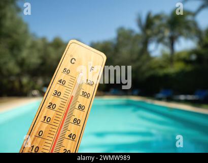 Holzthermometer mit roter Messflüssigkeit, die hohe Temperaturen an sonnigen Tagen auf dem Hintergrund des Schwimmbades anzeigt. Konzept von Urlaub, Urlaub, warm Stockfoto