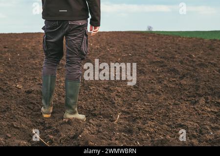 Männlicher Agronomist, der auf gepflügtem Ackerfeld steht, Rückansicht Stockfoto