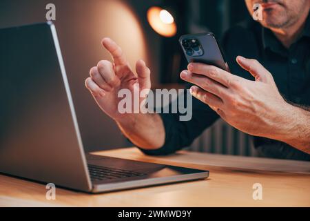 Geschäftsmann, der Laptop und Smartphone im Büro verwendet, während er Überstunden arbeitet, selektiver Fokus Stockfoto