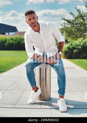 Man sieht einen Mann, der auf einem hohen Metallmast sitzt und vorsichtig balanciert, während er nach unten blickt. Die städtische Umgebung steht im Gegensatz zu seiner prekären Lage. Stockfoto