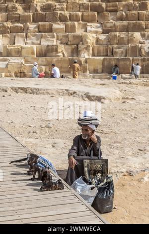 Gizeh Nekropolis, Ägypten - 26. April 2022: Alte Beduinen in traditioneller Kleidung, verkaufen spezifische Souvenirs vor der Gizeh Nekropolis Pyramide Stockfoto