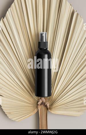 Schwarze Sprühflasche mit einem Palmblatt auf dem beigefarbenen Tisch. Stockfoto