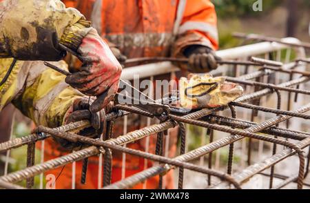 Ein Arbeiter verwendet Stahlbindedraht, um Stahlstäbe in Nahaufnahme an Verstärkungsstäben zu befestigen. Stahlbetonkonstruktionen - Herstellung eines Stahlverstärkungskäfigs f Stockfoto